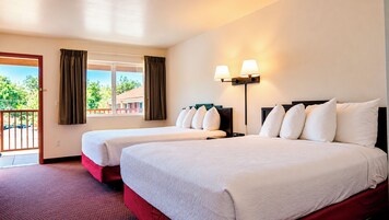 Habitación de hotel con dos camas, un balcón y vistas a la vegetación.