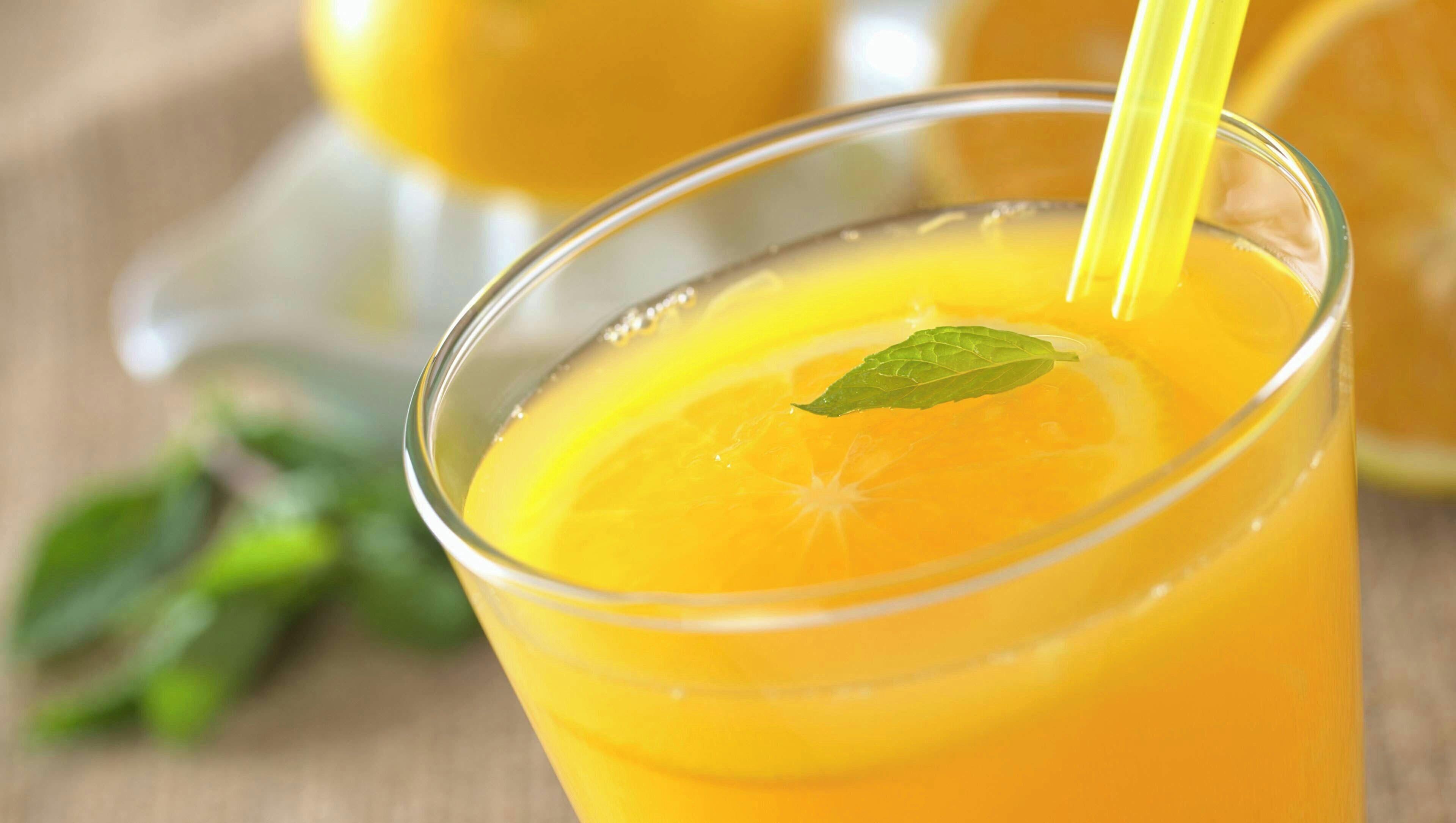 A glass of orange juice with a straw and a mint leaf garnish.