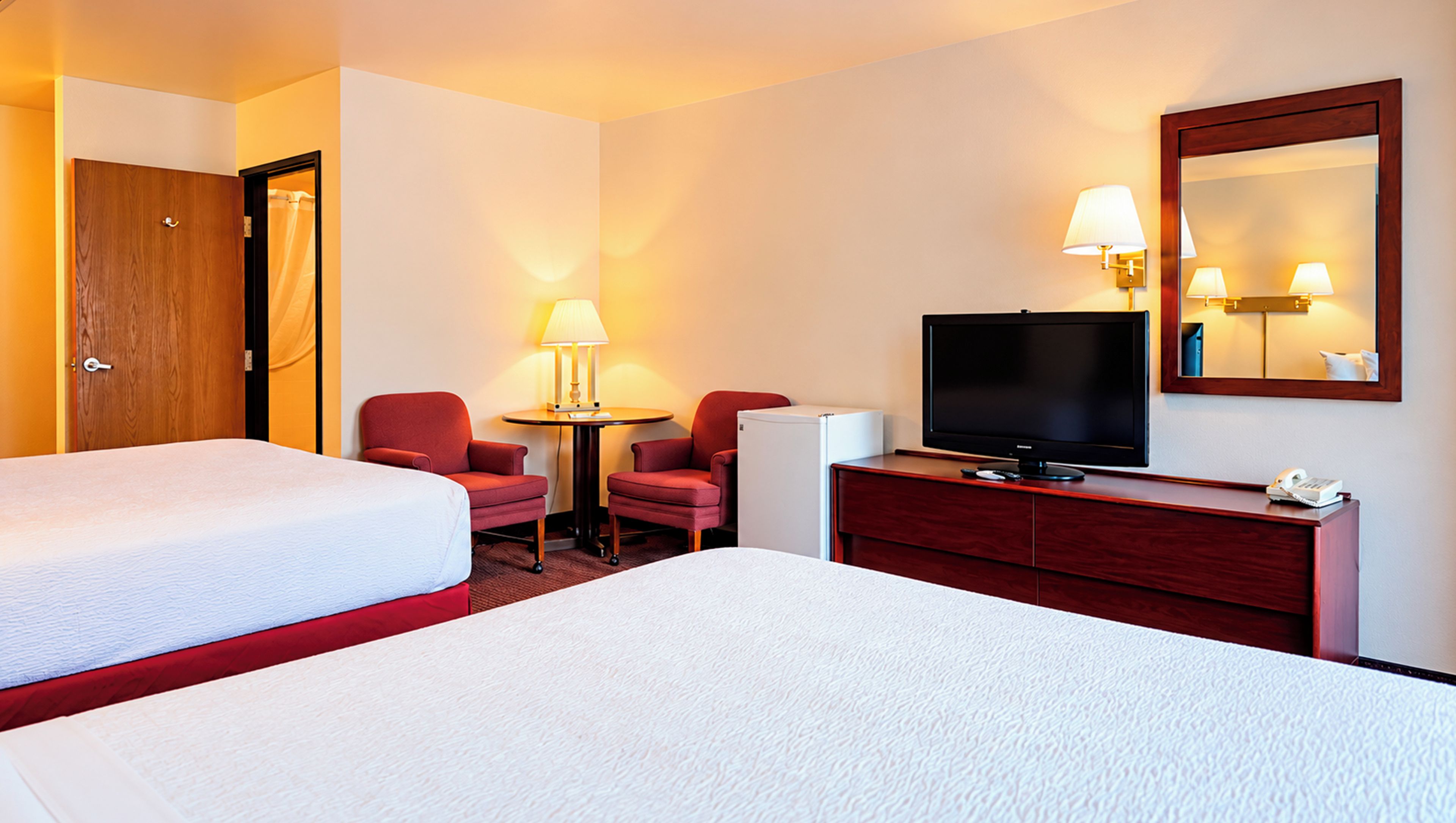 Une chambre d’hôtel avec deux lits, une télévision, un bureau avec une lampe et un miroir.