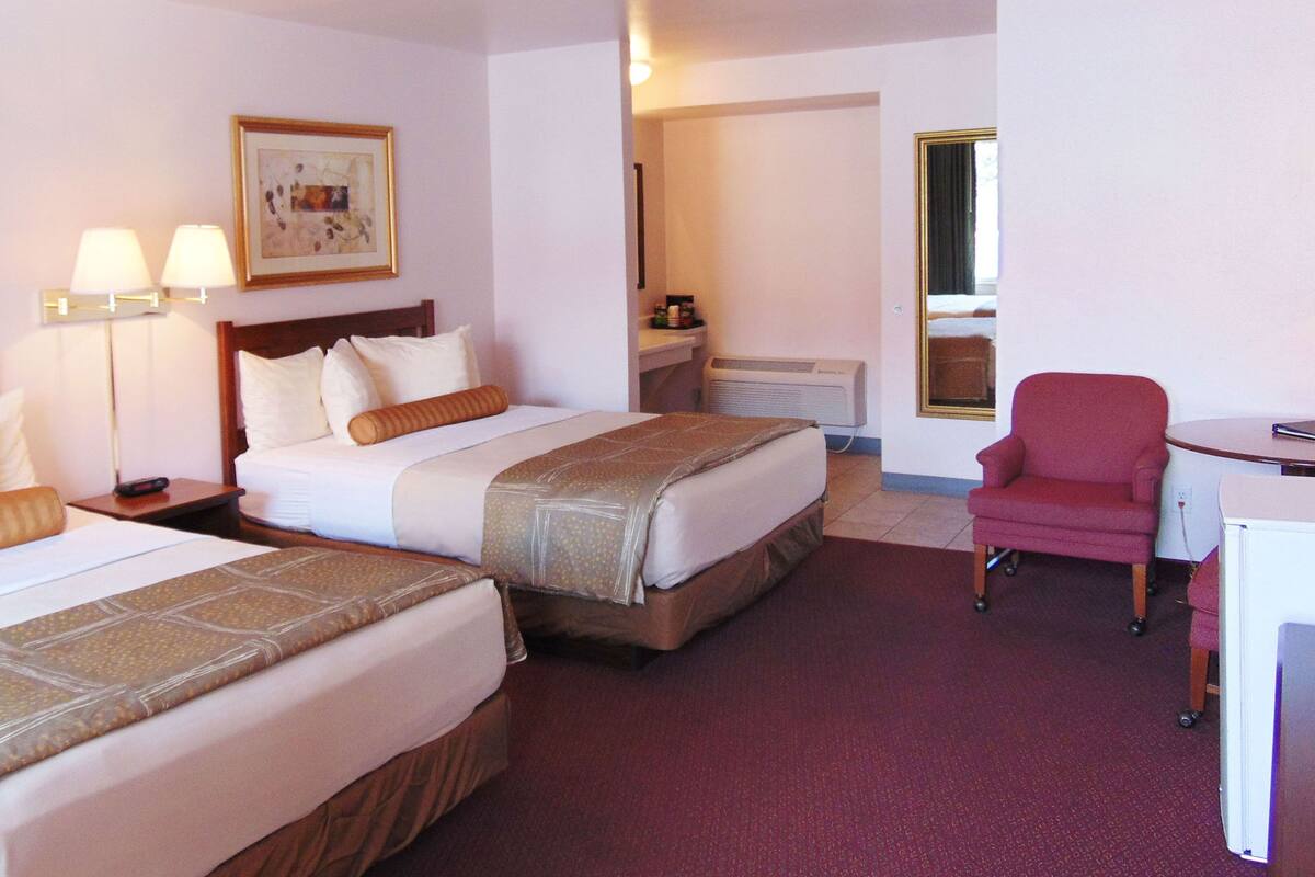 Habitació d'hotel amb dos llits, una taula, una cadira, una làmpada i un quadre a la paret.