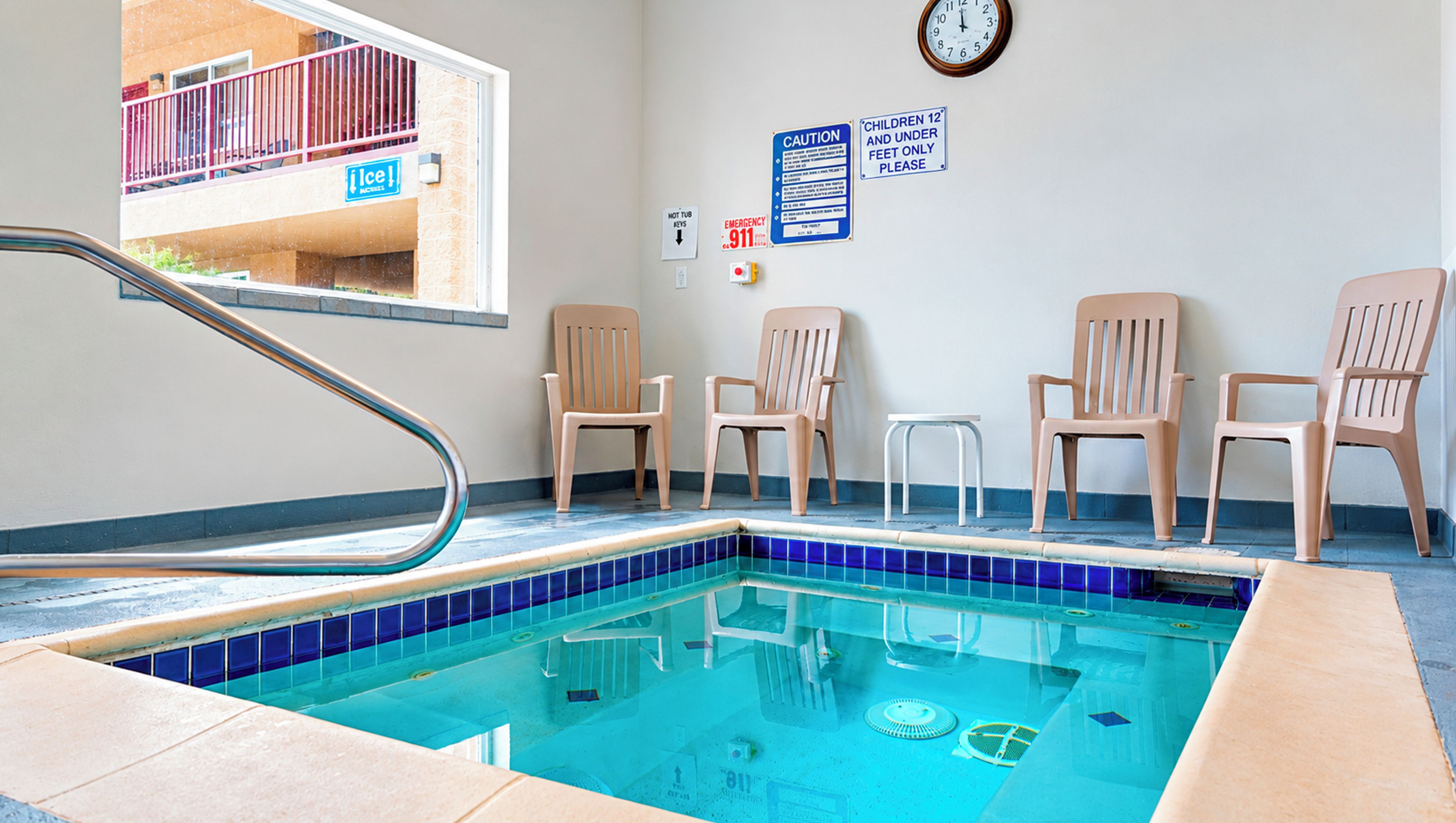 An indoor swimming pool with a pool ladder, chairs, and safety signs on the walls.