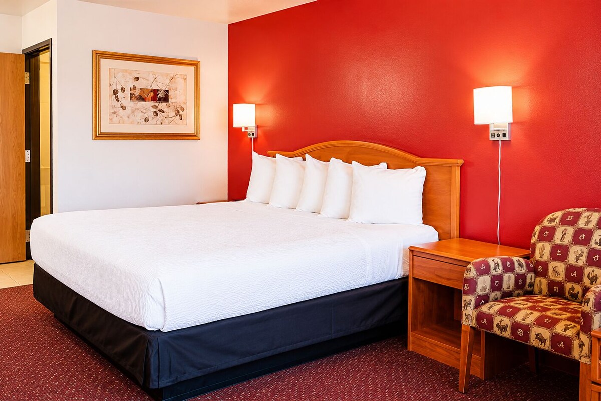 Une chambre d’hôtel comprenant un lit, une table de chevet, une chaise, une porte et un luminaire fixé au mur.