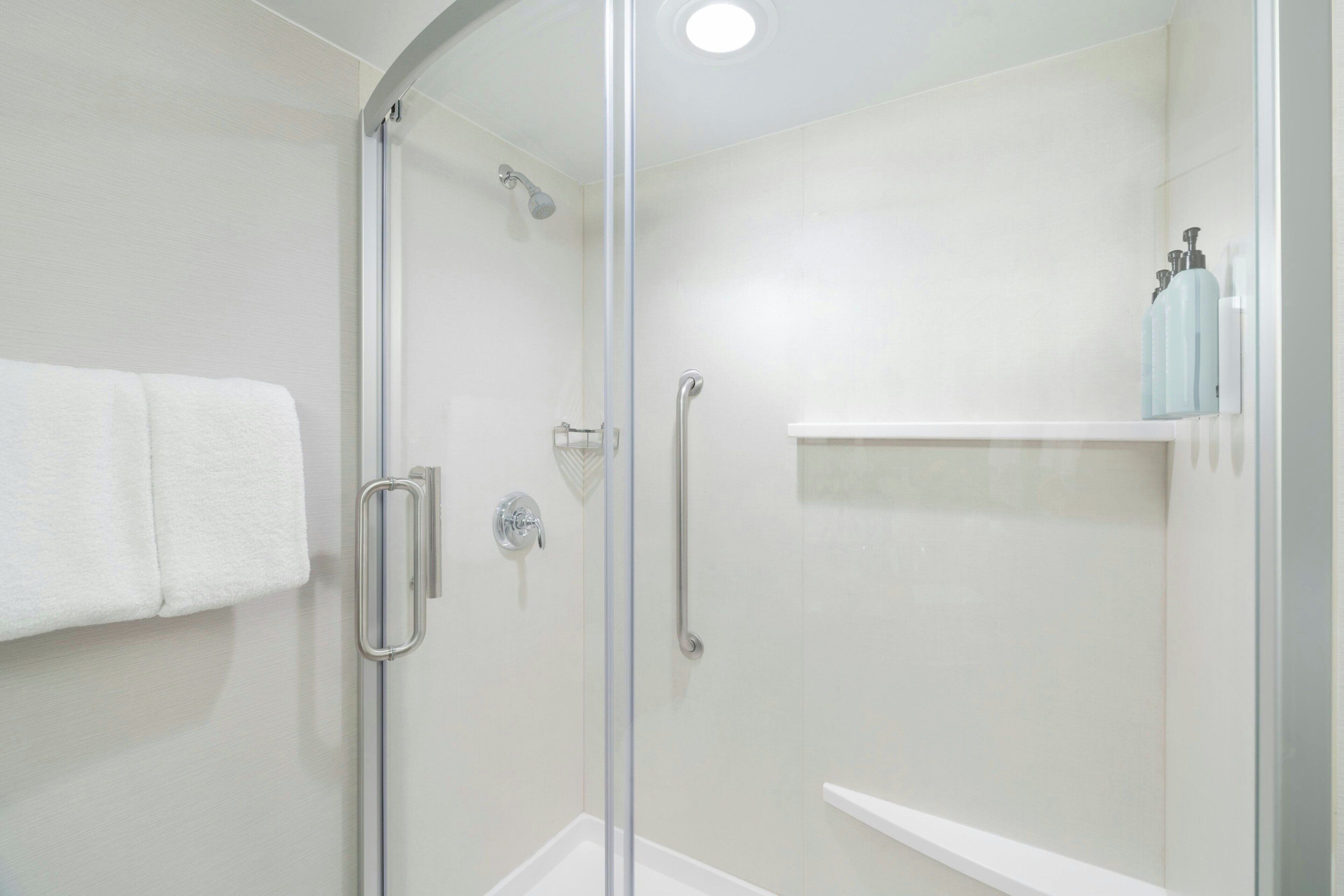 Une salle de bain moderne avec une douche à parois de verre, une serviette blanche accrochée au mur et une étagère contenant des articles de toilette.