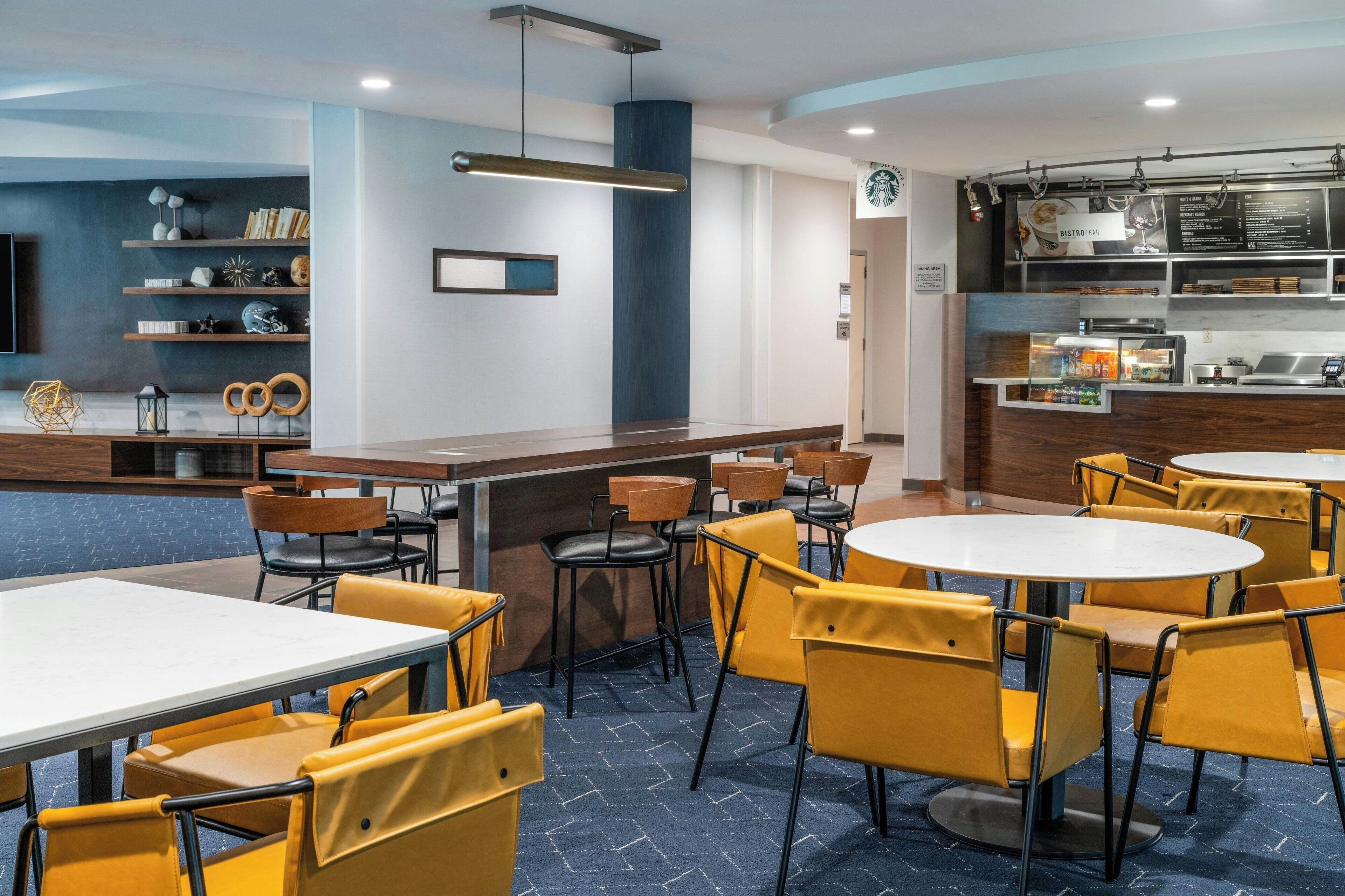A modern restaurant with round tables and yellow chairs, a bar area, and a menu display.