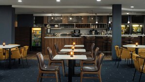 En modern restaurang med flera bord och stolar, en bardisk och ett kylskåp fyllt med drycker.
