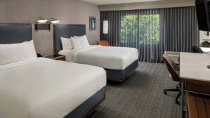 Ett hotellrum med två sängar, ett skrivbord, en stol, en TV och ett fönster med gardiner.