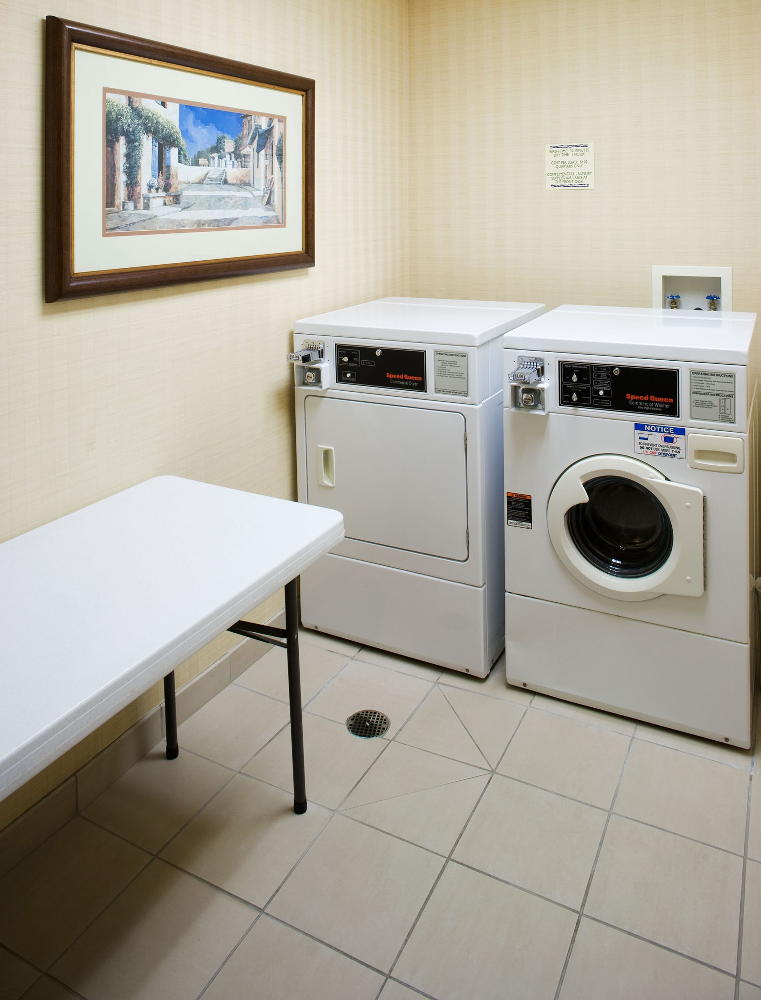 A laundry room with two stacked washers and dryers, a framed painting on the wall, and a white table.