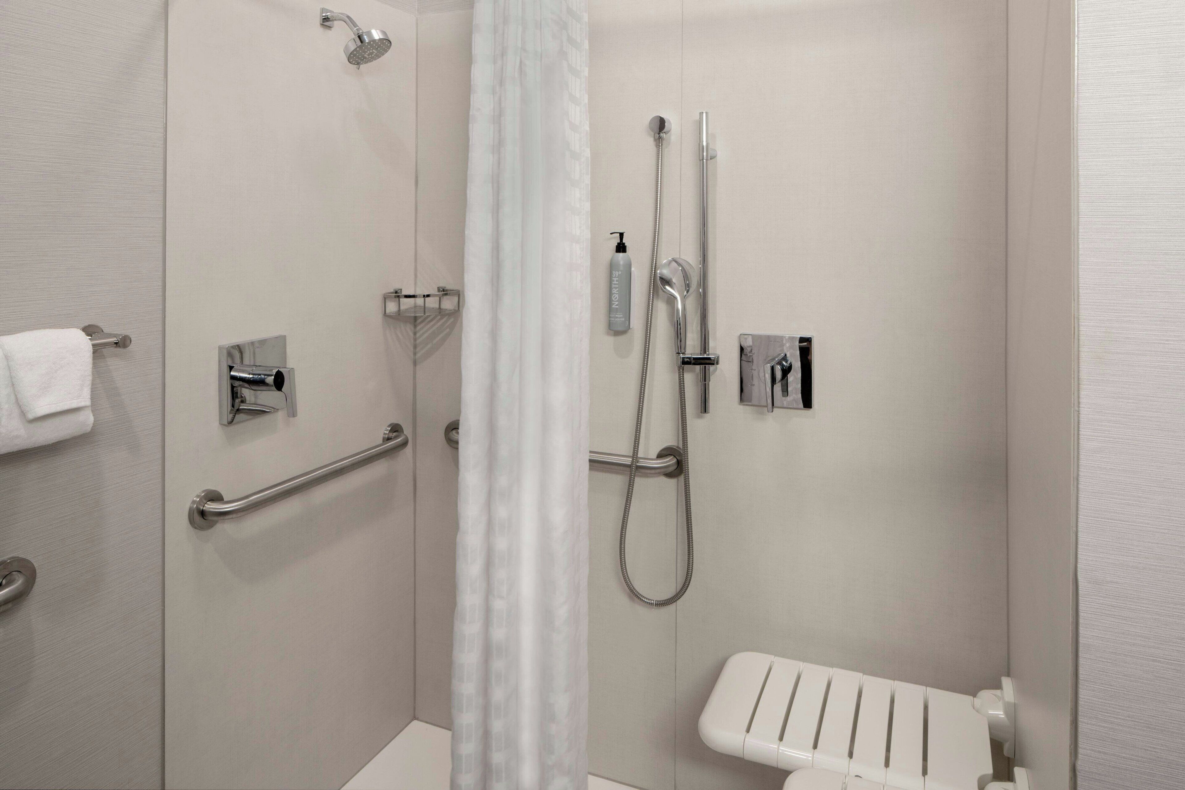A modern bathroom with a shower, grab bar, and a white toilet.