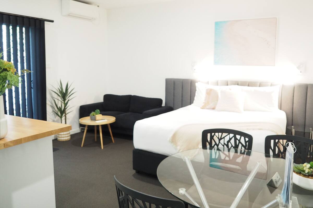 A hotel room with a bed, a sofa, a glass table, and a small side table.