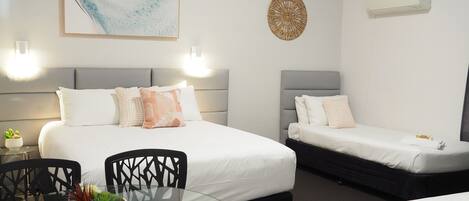Une chambre d’hôtel avec deux lits, une table en verre avec des chaises, un climatiseur fixé au mur et un élément décoratif mural.