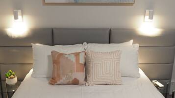 A neatly made bed with two pillows, a small plant on a bedside table, and a wall-mounted light fixture.