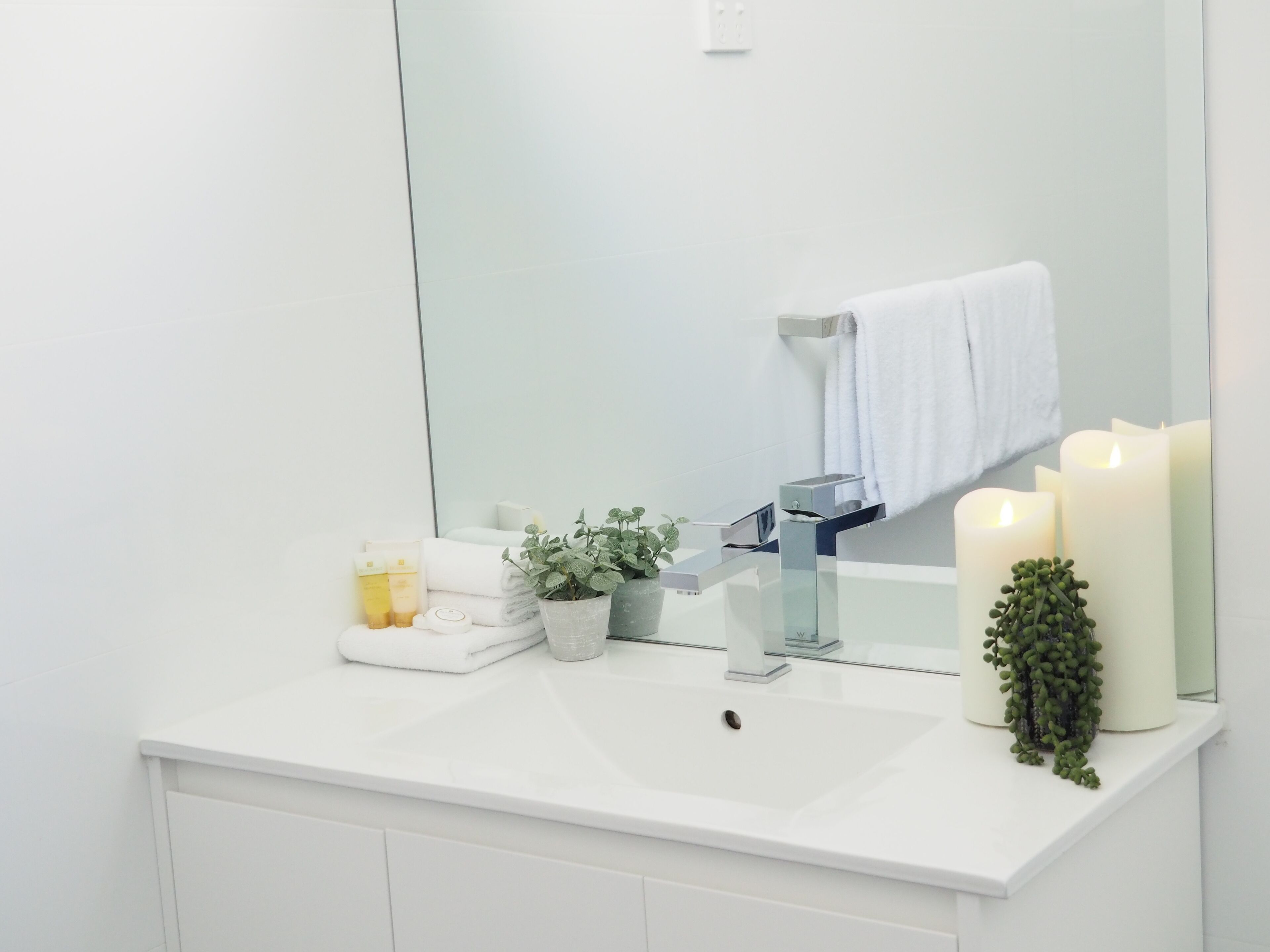 Un baño moderno con un lavamanos blanco, un espejo y tres velas encendidas.