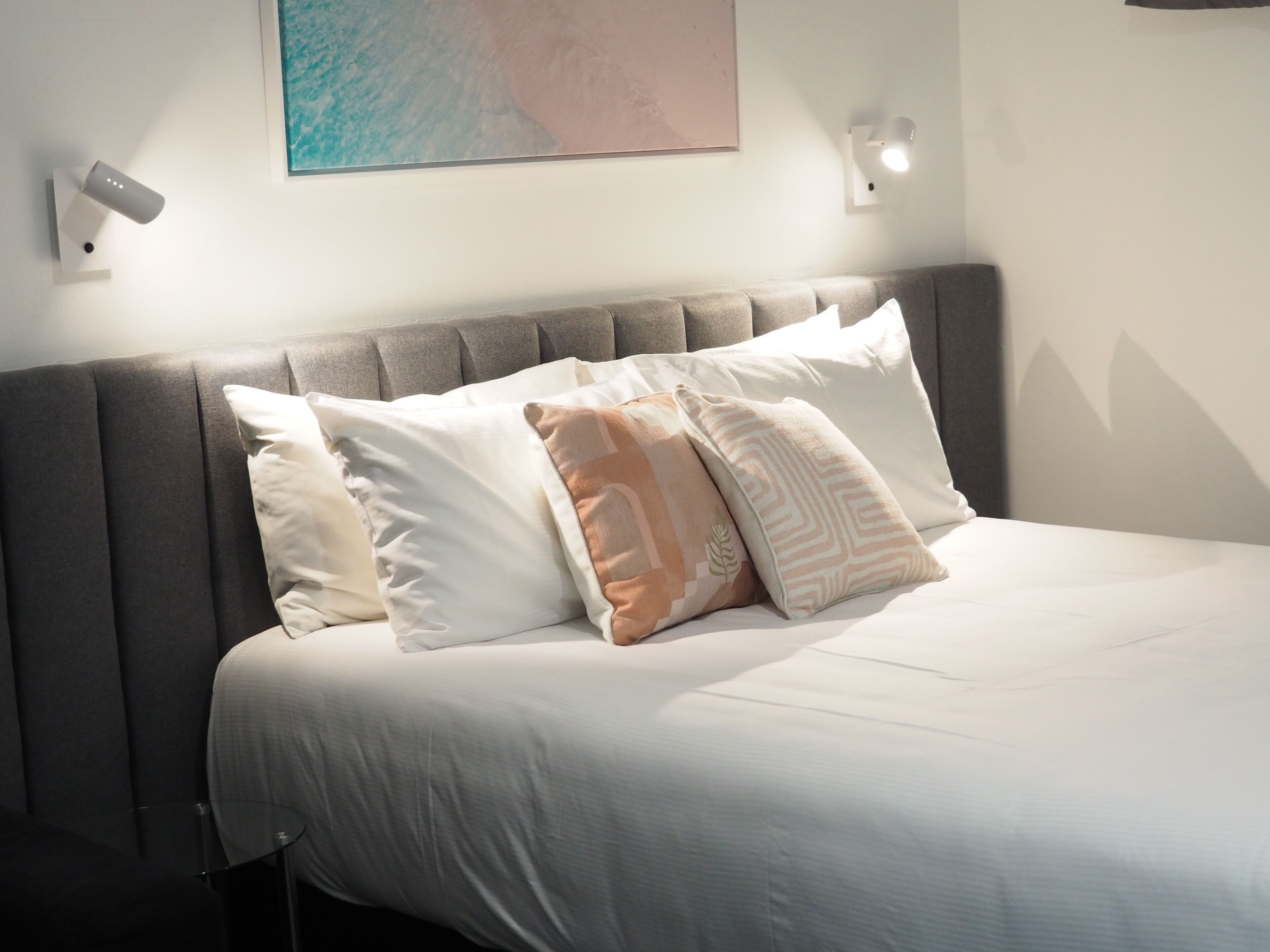 Een net opgemaakt bed met een grijze hoofdbord, witte beddengoed en decoratieve kussens.