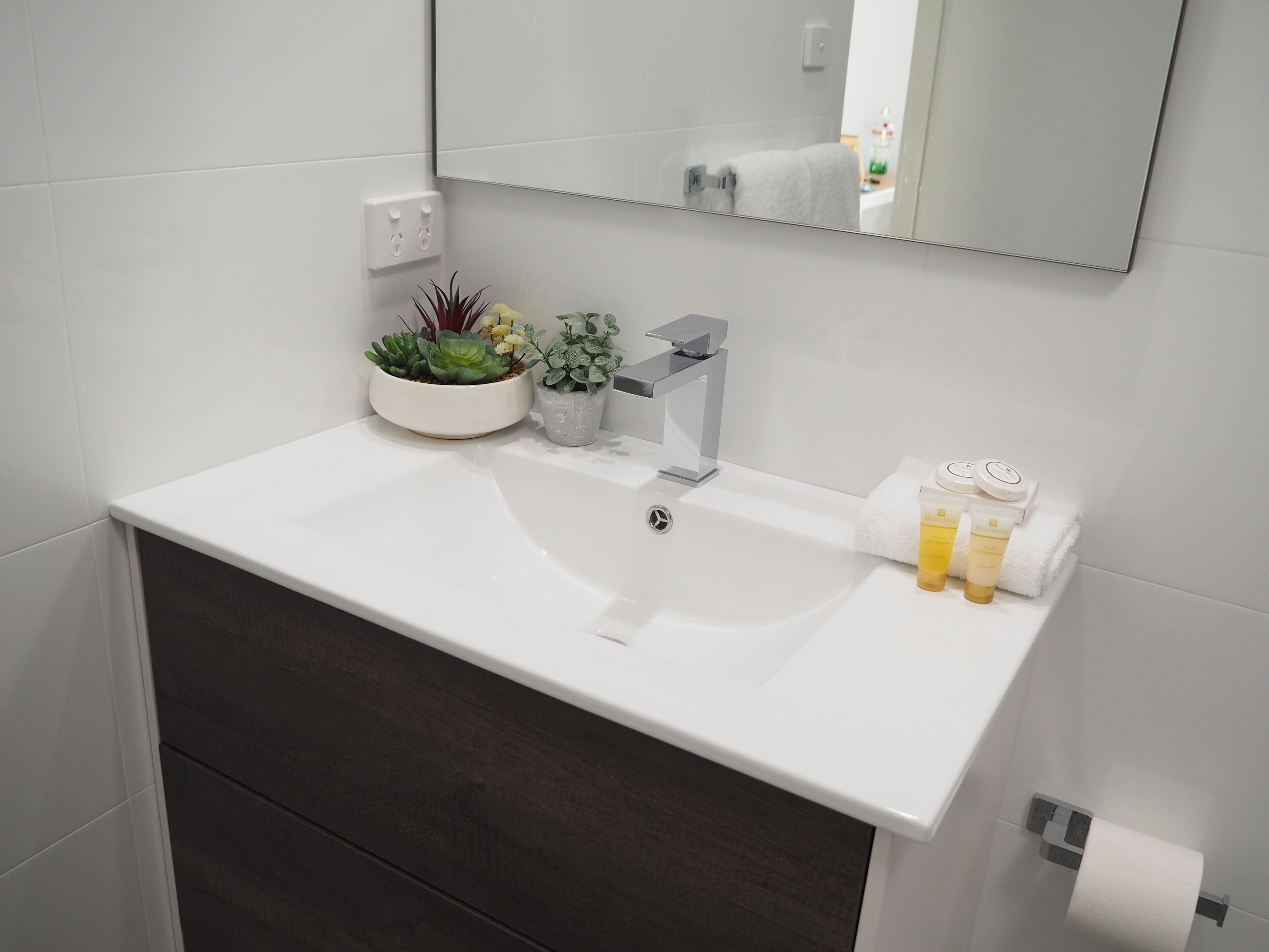 Une salle de bain avec un lavabo blanc, un miroir, un porte-serviettes et un support à papier toilette.