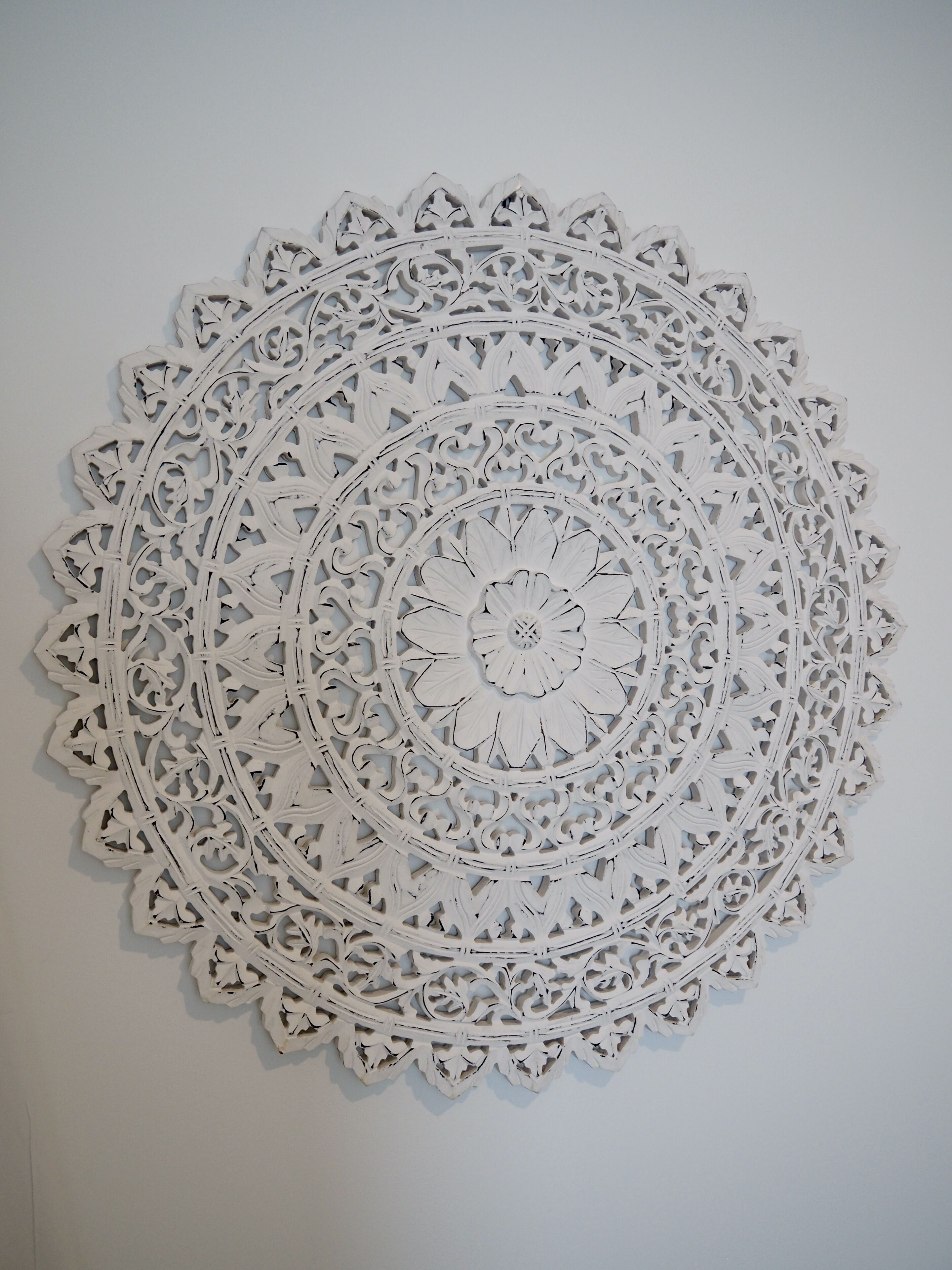 A white, intricately designed wall hanging with a circular pattern.