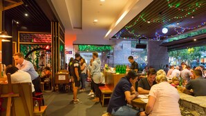 A busy indoor dining area with tables and chairs, a counter, and a sign that reads "Please wait to be seated." - The Esplanade Motel (Warners Bay)
