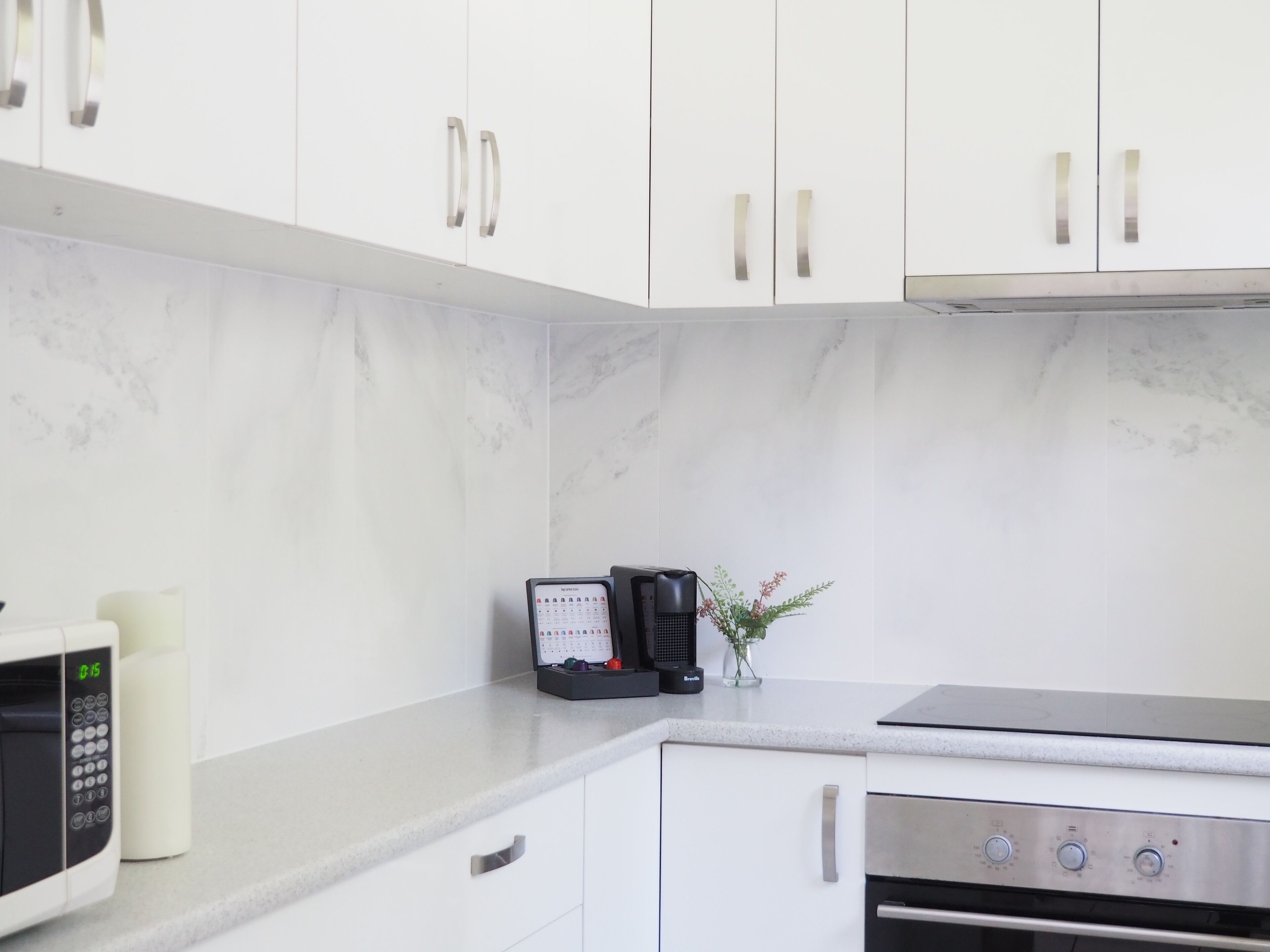 A kitchen with white cabinets, a microwave, a coffee maker, and a small potted plant.