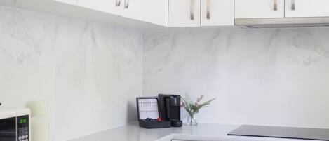 A kitchen with white cabinets, a microwave, a coffee maker, and a small potted plant.