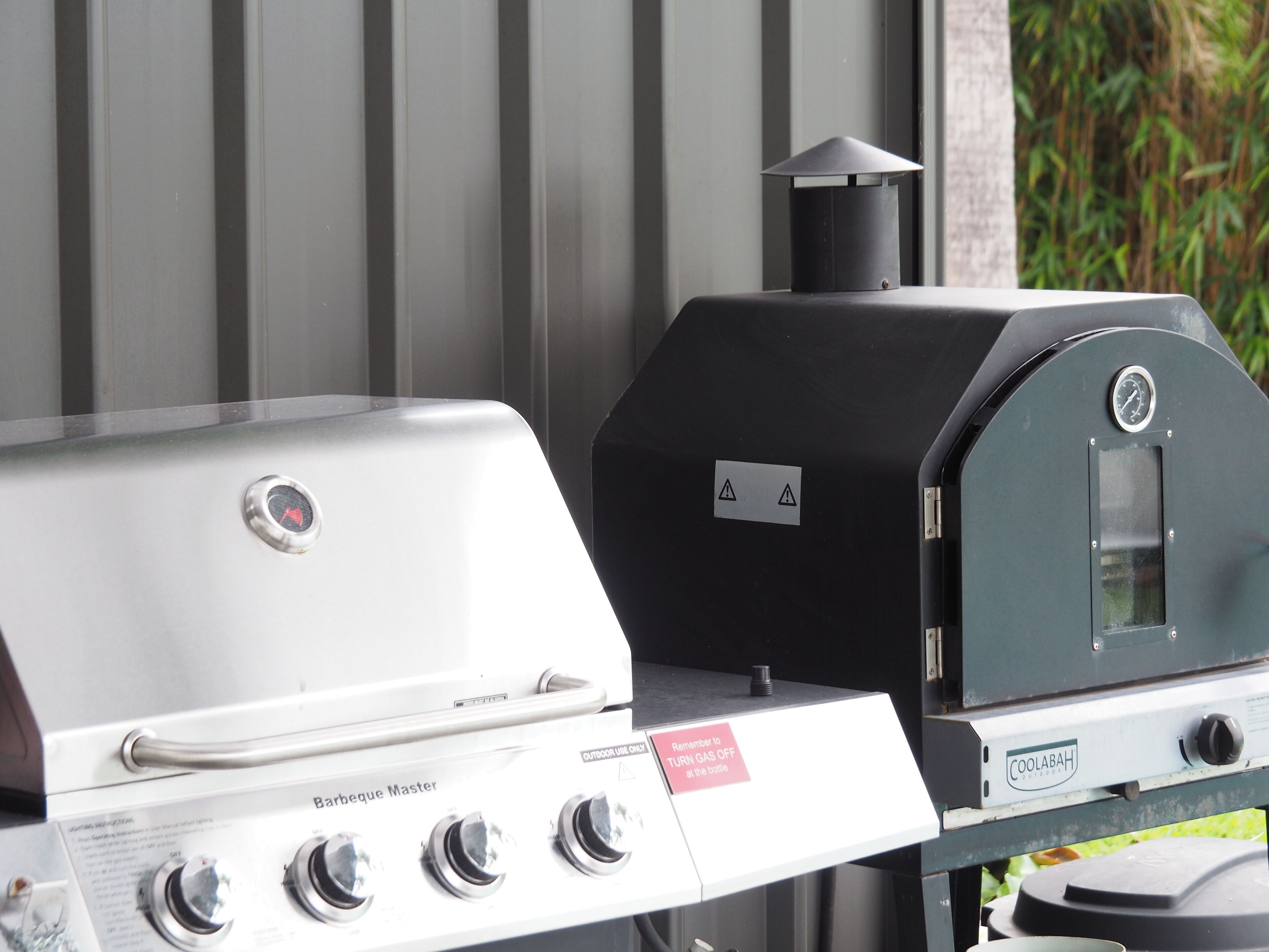 A barbecue grill with a white gas stove and a black charcoal grill, both with control knobs and a safety warning label.