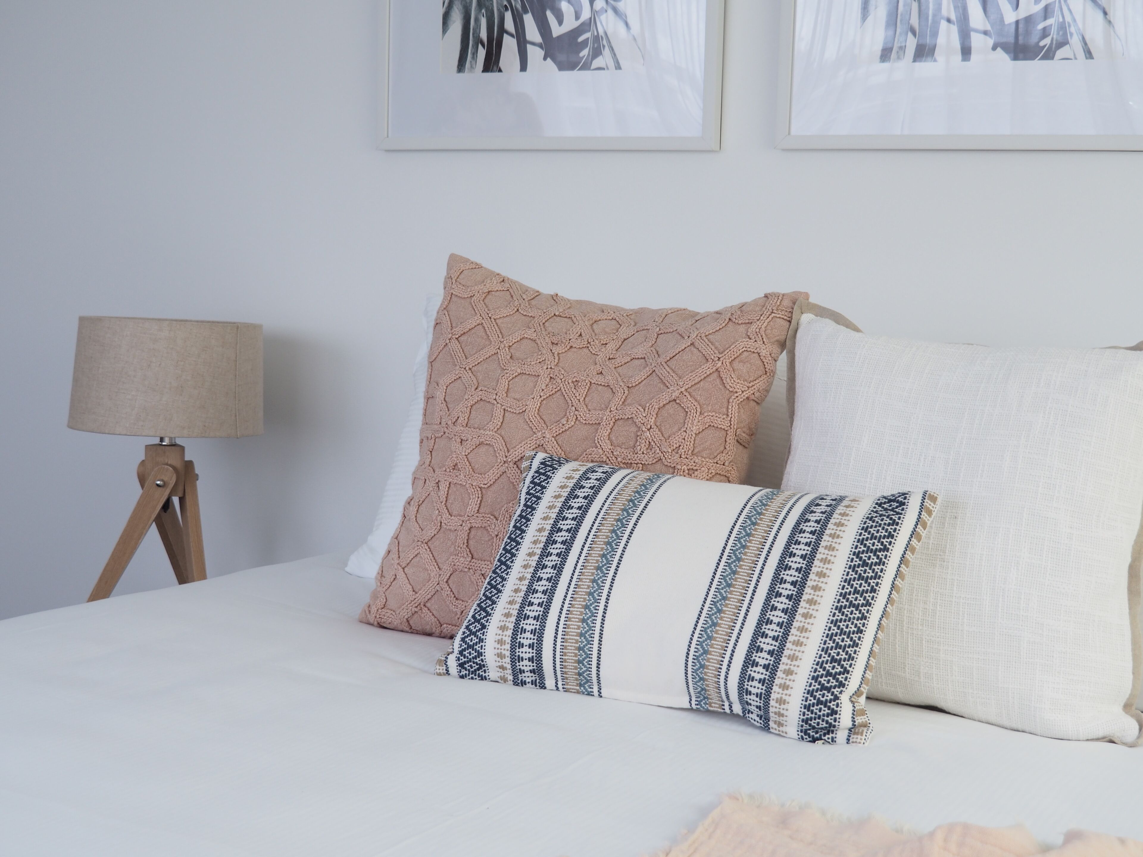 A bed with three pillows, a bedside lamp, and two framed pictures on the wall.