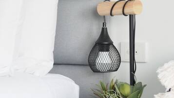 Ein ordentlich eingerichtetes Schlafzimmer mit einem grauen Sofa, weißen Kissen, einem kleinen Nachttisch mit Topfpflanze und einer Pendelleuchte.