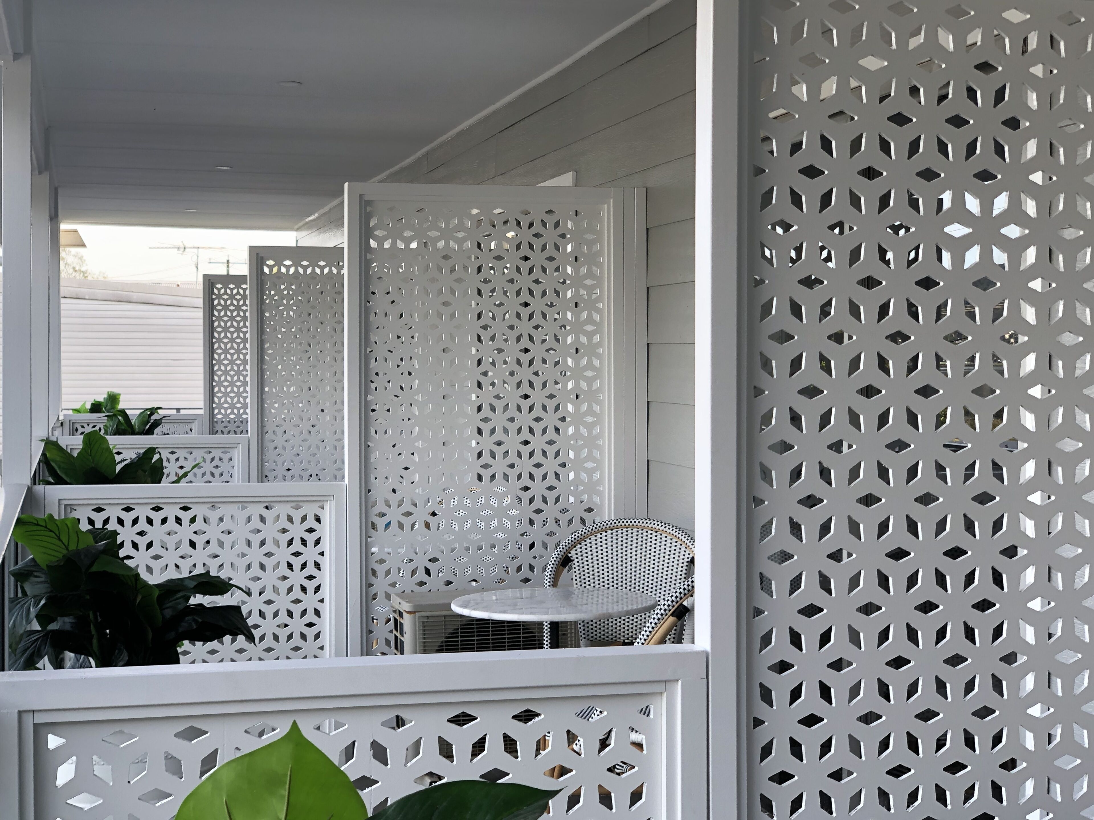 Een wit terras met een ronde tafel en stoelen, omgeven door witte lattenpanelen.