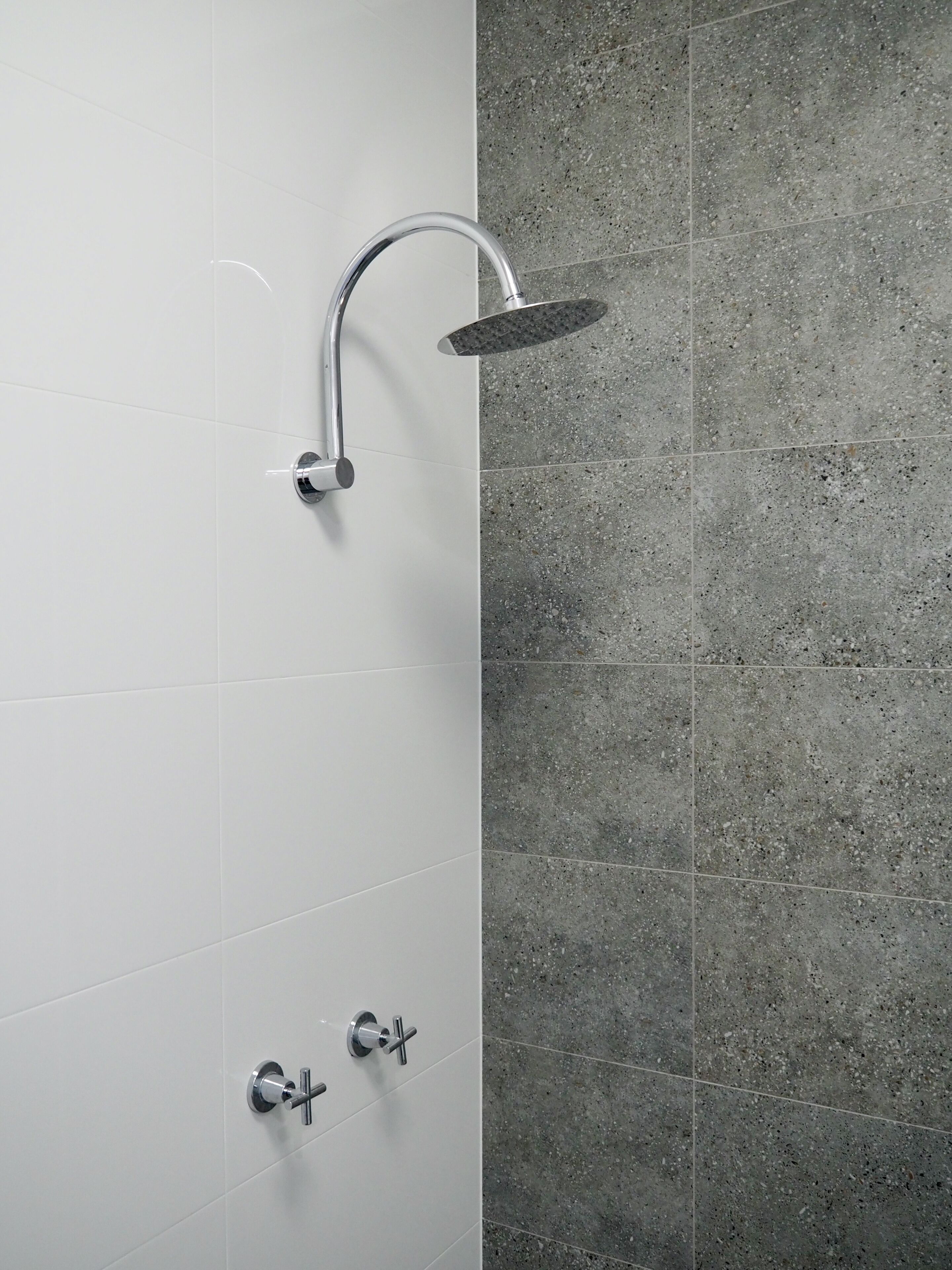 Una ducha moderna con grifo curvo y panel de control en la pared.