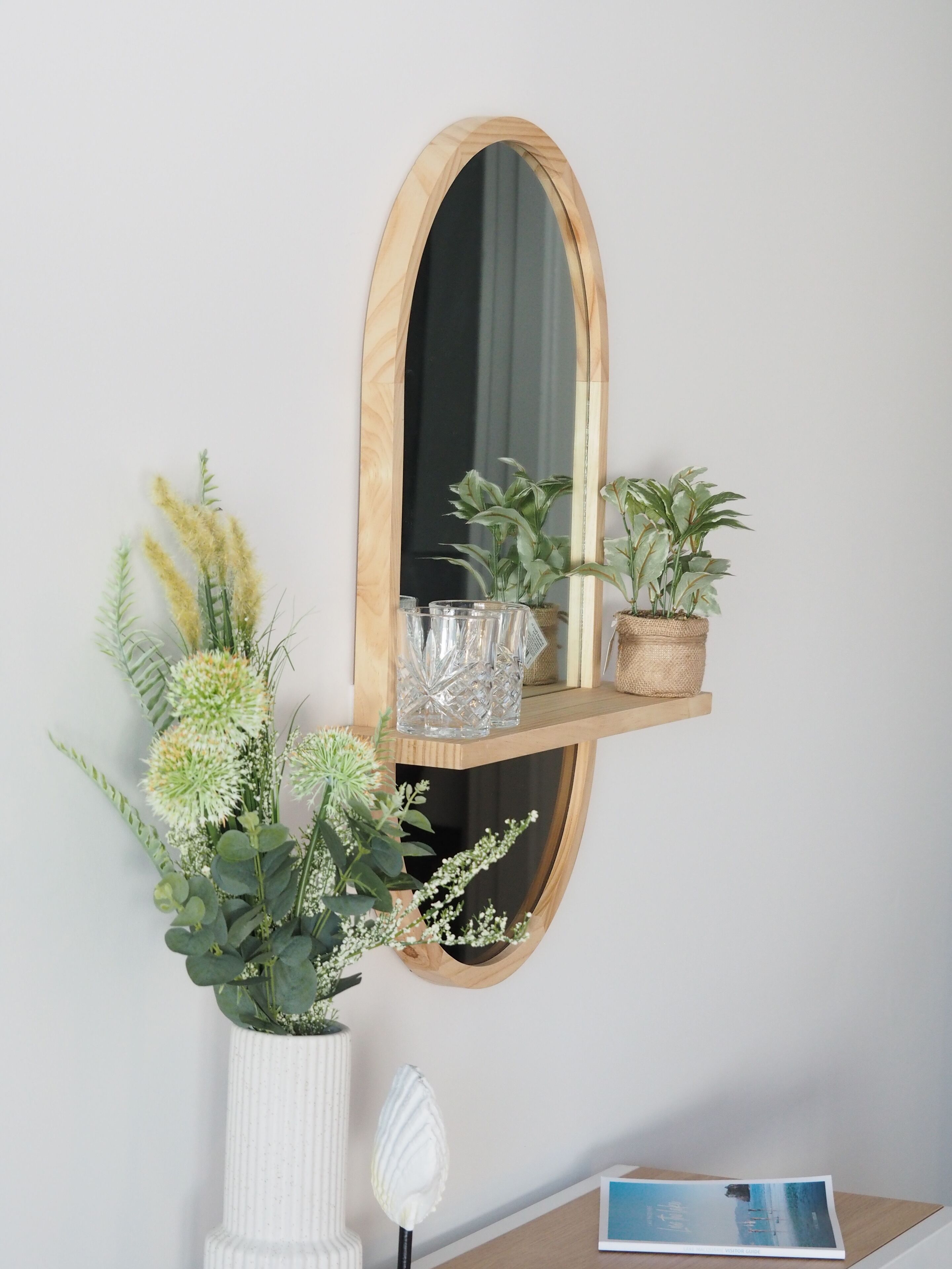 A wall-mounted wooden shelf with decorative items, a mirror, and a small table with a book.