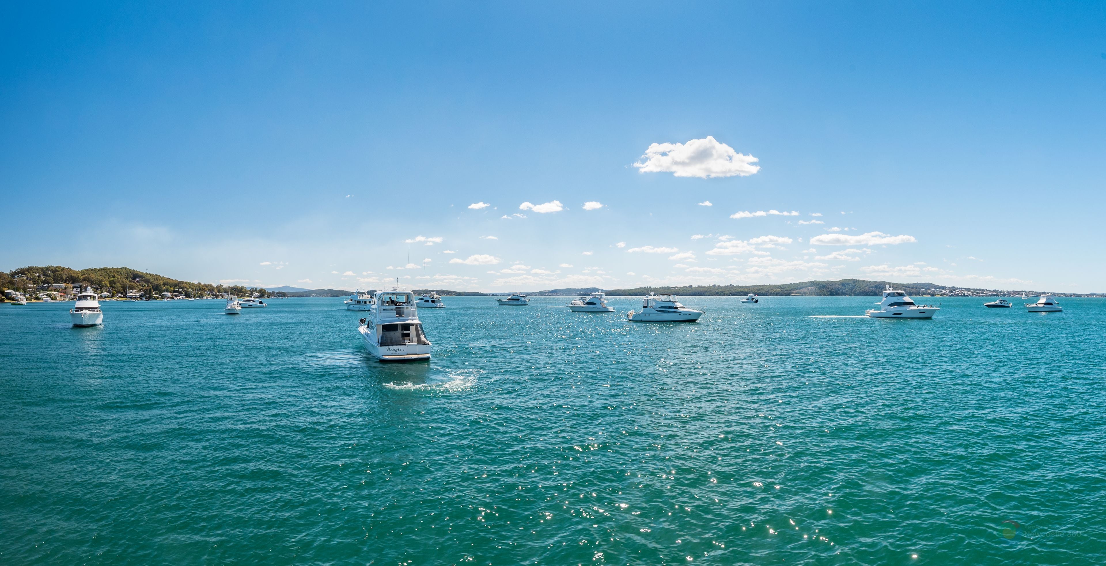 A marina with multiple boats docked, calm water, and a clear sky.
