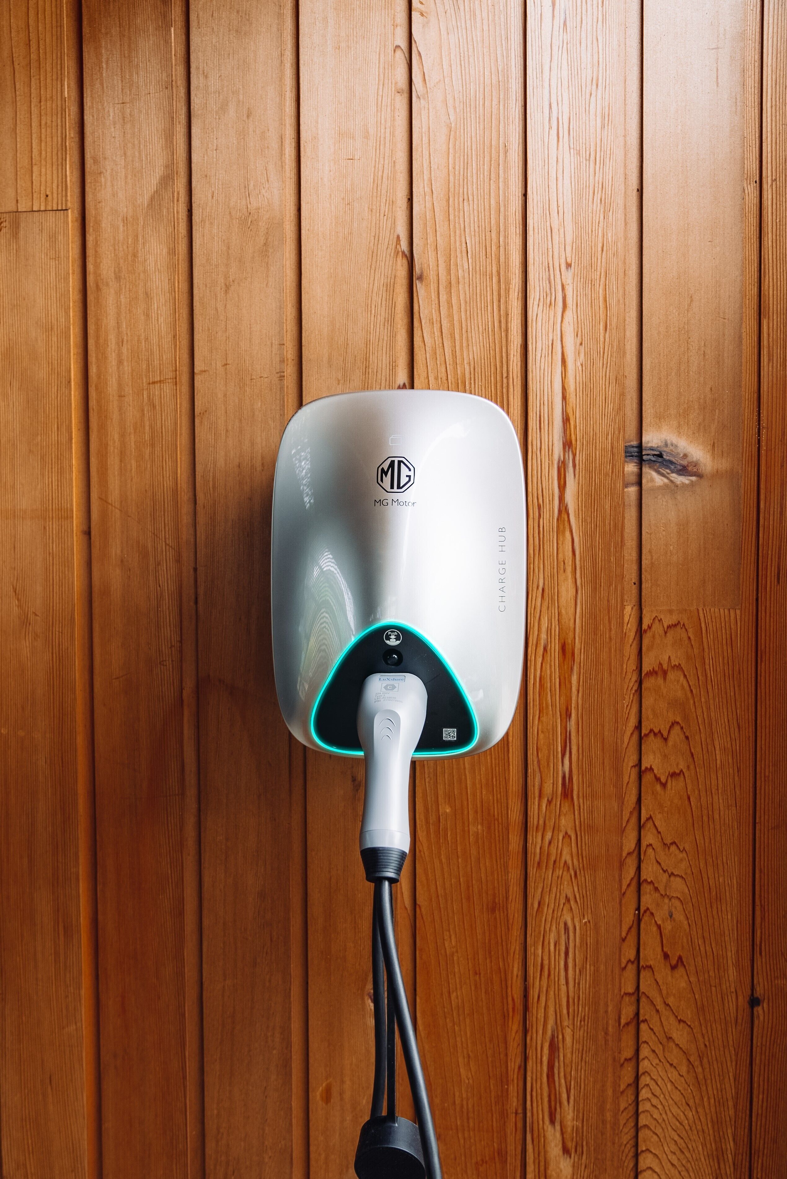 A wall-mounted electric vehicle charging station with a visible logo and the text "MG Motor" and "CHARGE HUB".