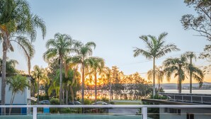 A view of a coastal area with palm trees and a sunset in the background. - The Esplanade Motel (Warners Bay)