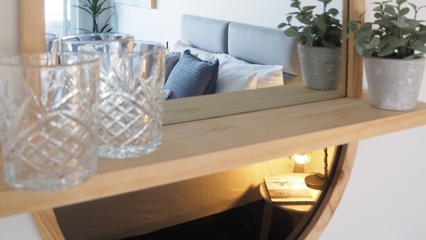 A mirror with a wooden frame, a decorative wall piece, and a shelf with glassware and potted plants. - The Esplanade Motel (Warners Bay)