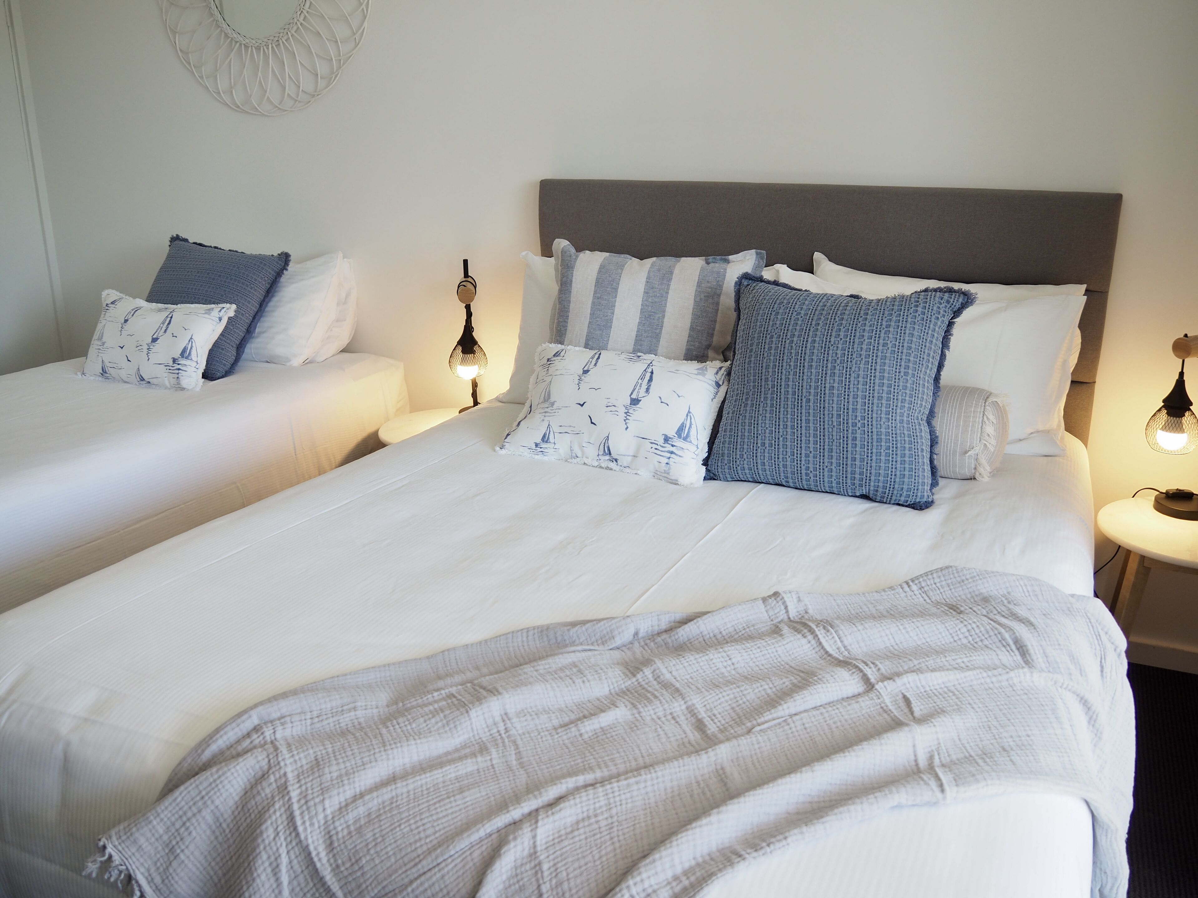 A hotel room with two single beds, each with a headboard, bedside tables, and lamps.