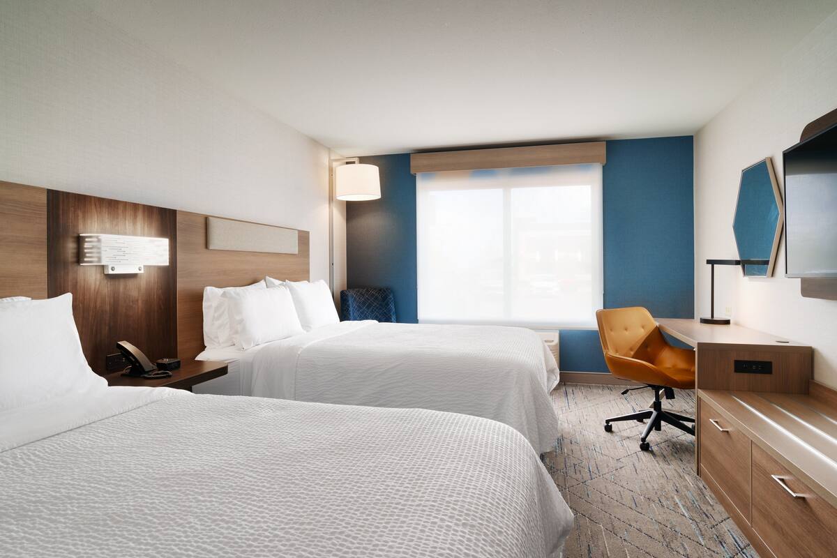 A hotel room with two beds, a desk, a chair, and a large window.