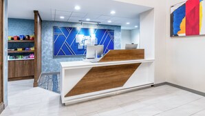 A reception area with a modern design, featuring a reception desk, a blue geometric wall, and a wooden shelf with snacks. - Holiday Inn Express Hotel & Suites - Cheyenne by IHG (Cheyenne)
