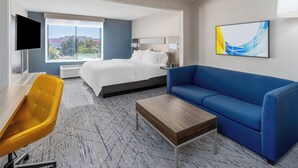 A hotel room with a bed, a blue sofa, a wooden coffee table, a yellow chair, and a TV on the left wall. - Holiday Inn Express Hotel & Suites - Cheyenne by IHG (Cheyenne)