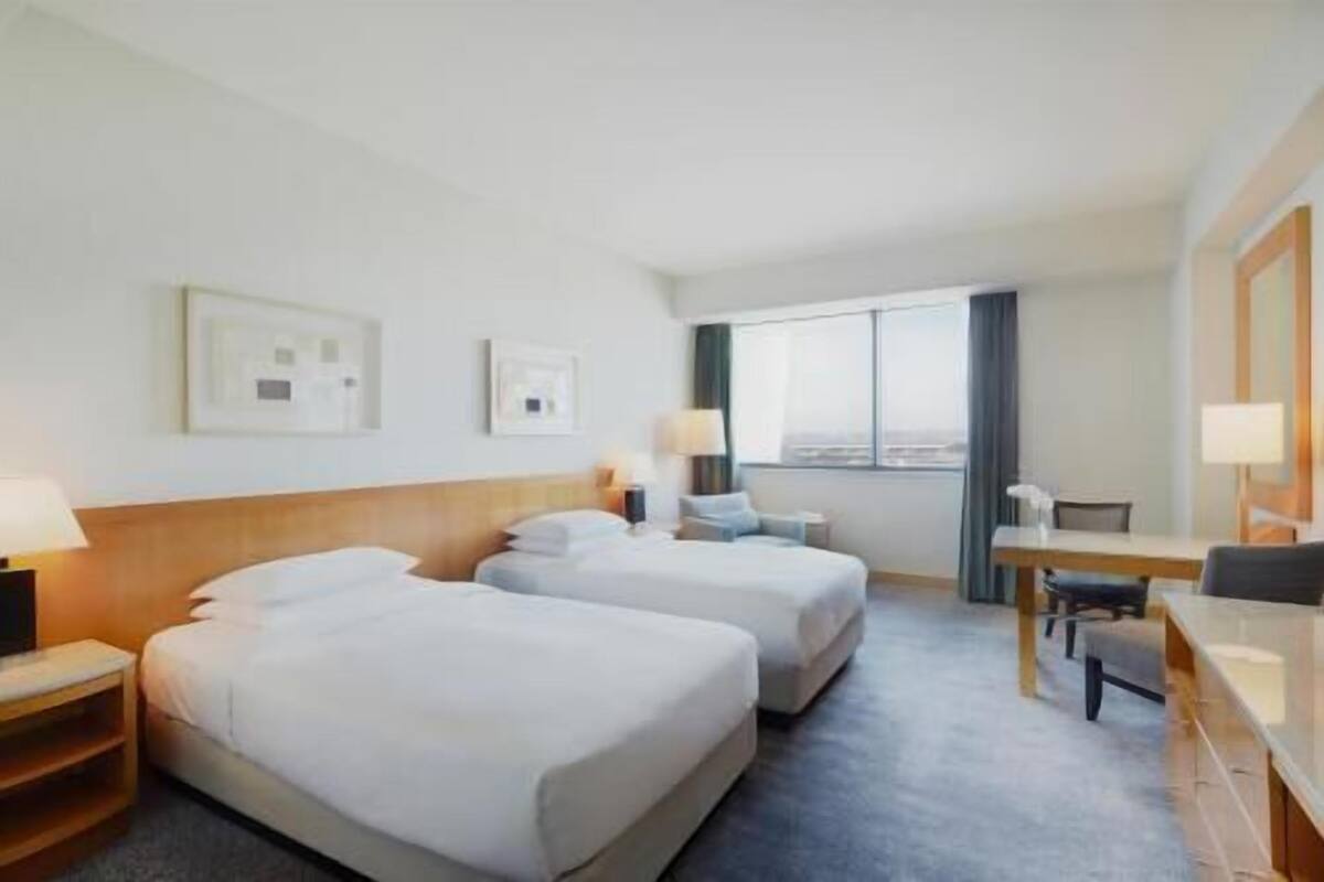 Une chambre d’hôtel avec deux lits, un bureau, une chaise et une fenêtre donnant sur un paysage agréable.
