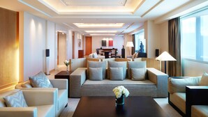 A hotel room with a sofa set, a coffee table, a TV, and a dining area with a table and chairs.