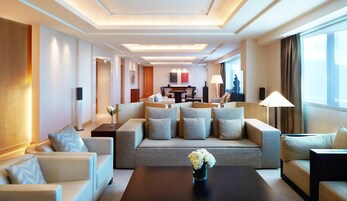 A hotel room with a sofa set, a coffee table, a TV, and a dining area with a table and chairs.