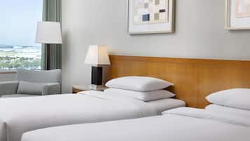 A hotel room with two beds, a nightstand with a lamp, a chair, and framed artwork on the wall.