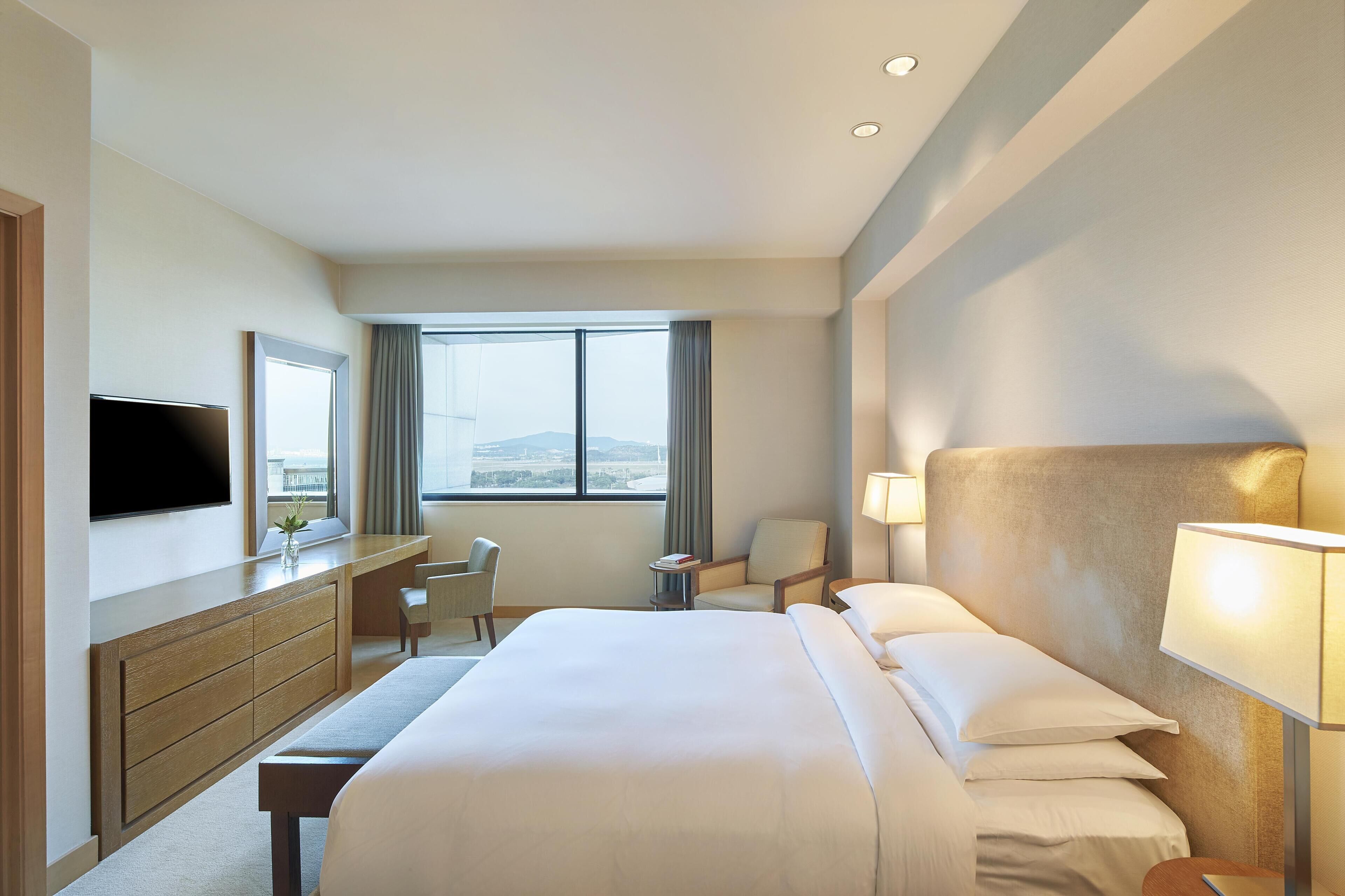A hotel room with a bed, a desk, a chair, a TV, and a window with a view.