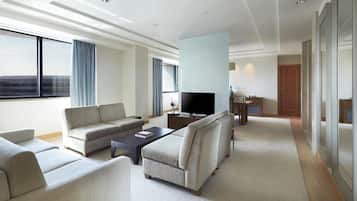 A modern hotel room with a sofa, armchairs, a coffee table, a TV, and a small dining area.