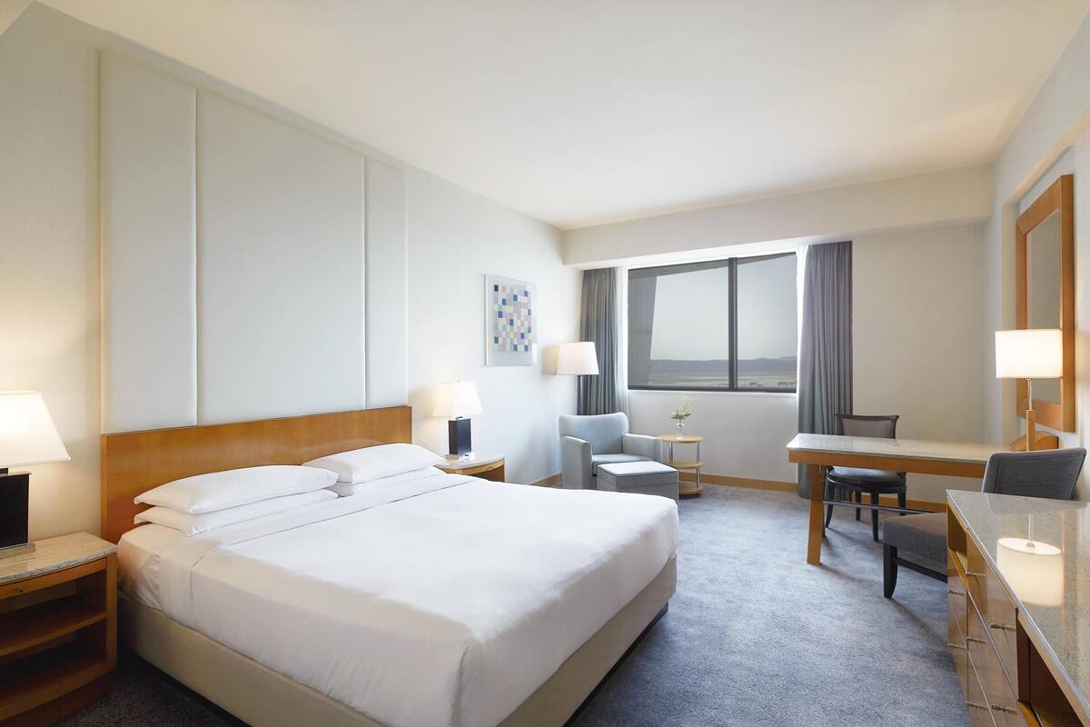 Une chambre d’hôtel avec un grand lit, un bureau, une chaise et une vue sur l’extérieur.