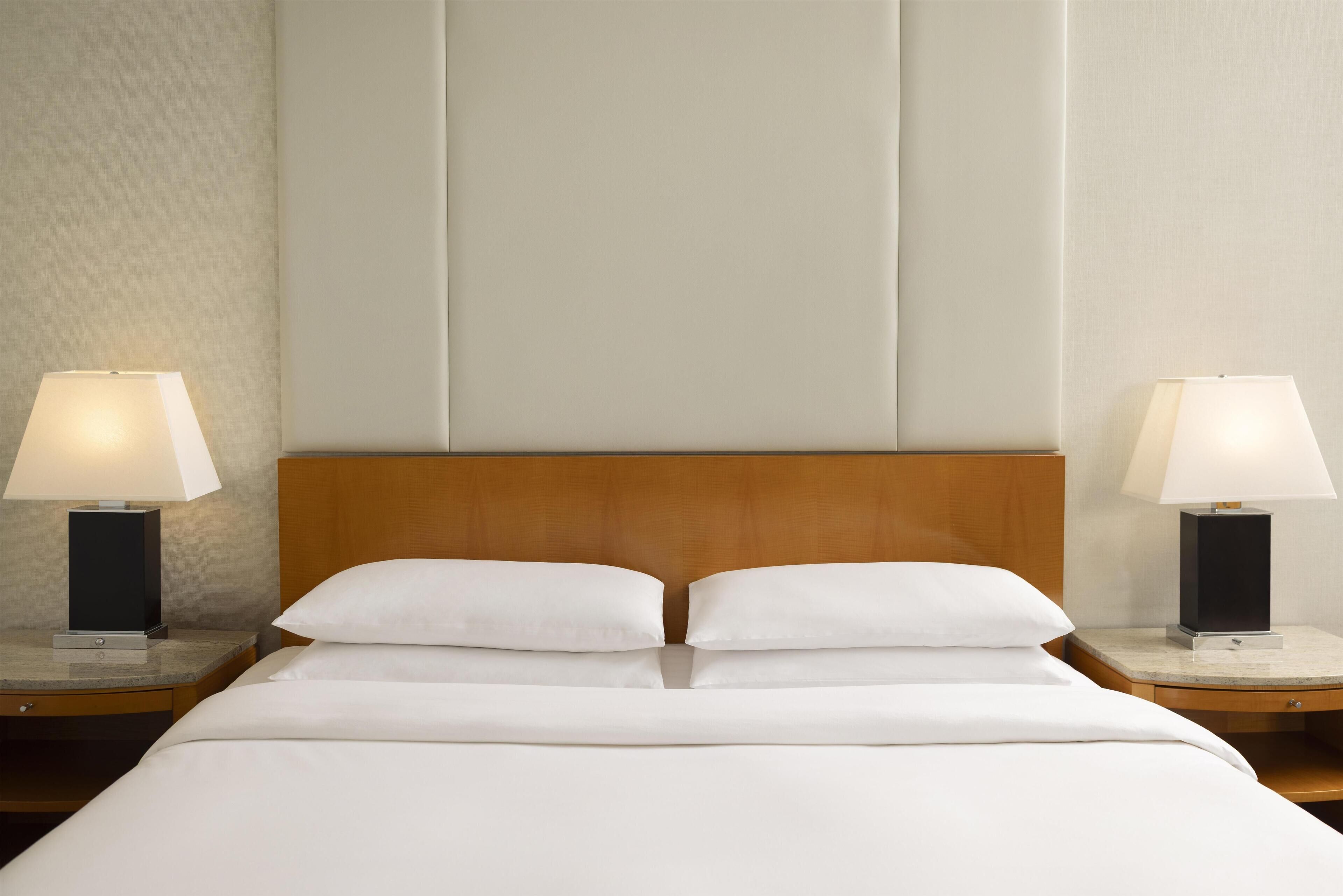 A hotel room with a wooden headboard, two bedside tables with lamps, and a neatly made bed with white linens.