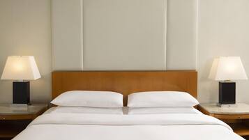 A hotel room with a wooden headboard, two bedside tables with lamps, and a neatly made bed with white linens.