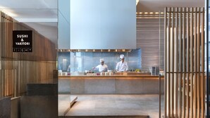 A modern sushi bar with a wooden design, a sign for 'SUSHI & YAKITORI,' and a view of chefs preparing food.