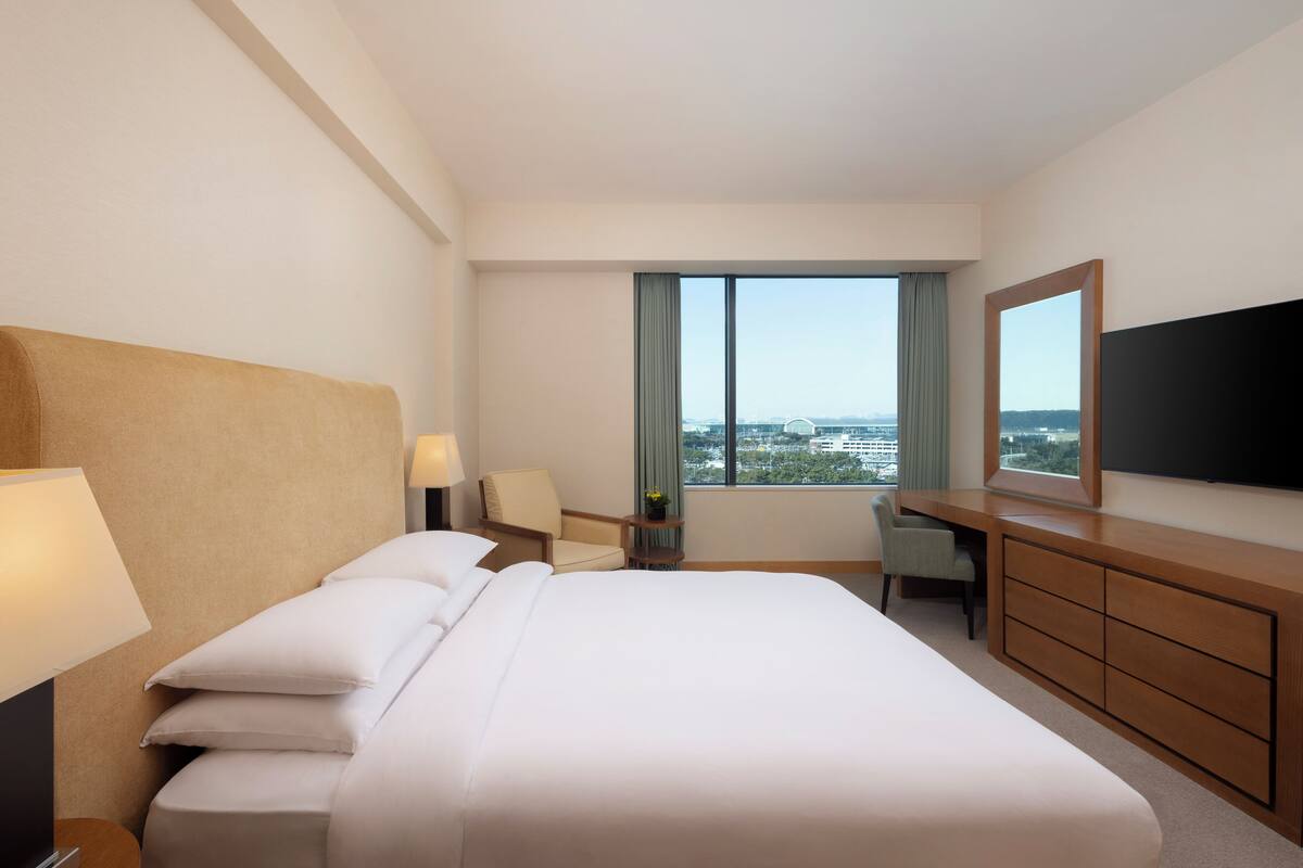 Une chambre d’hôtel avec un grand lit, un bureau, une chaise, une télévision et une fenêtre donnant sur la ville.