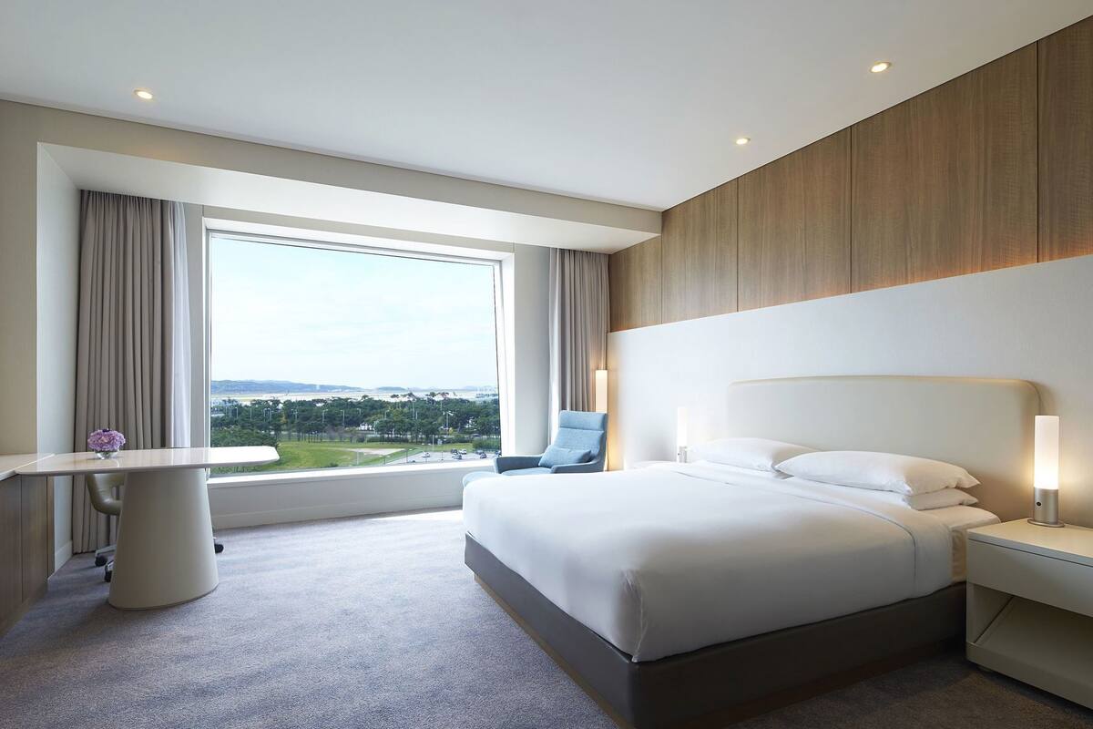 Une chambre d’hôtel avec un grand lit, un bureau, une chaise et une vue sur l’extérieur.