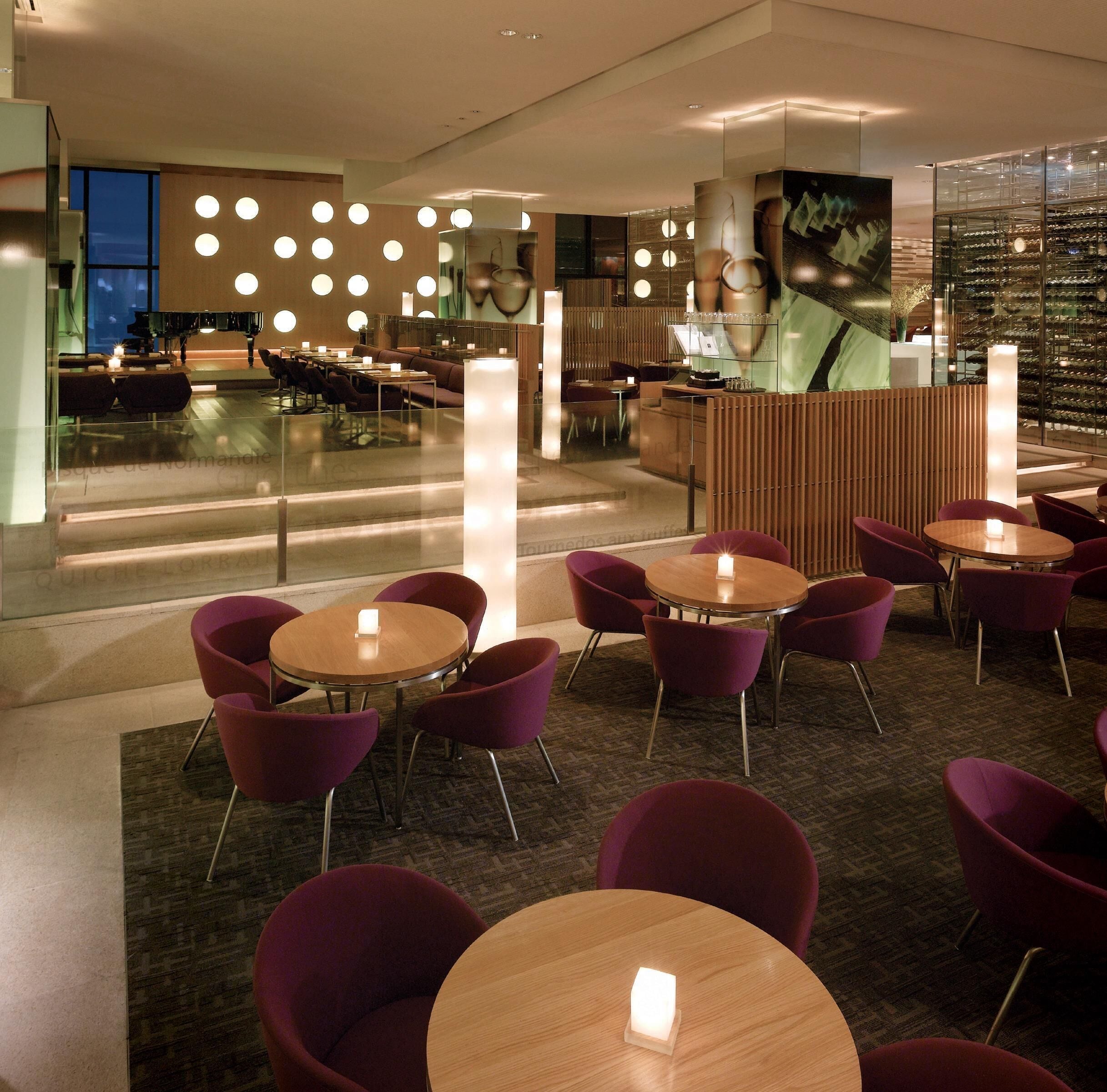 A modern hotel lobby with round tables, purple chairs, and a reception desk.