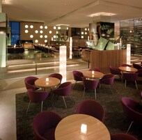 A modern hotel lobby with round tables, purple chairs, and a reception desk.